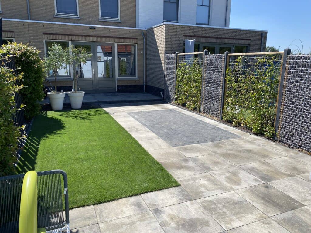 Ruime tuin met sierbestrating, gazon en tuinmuren met groen, kunstgras en planten.