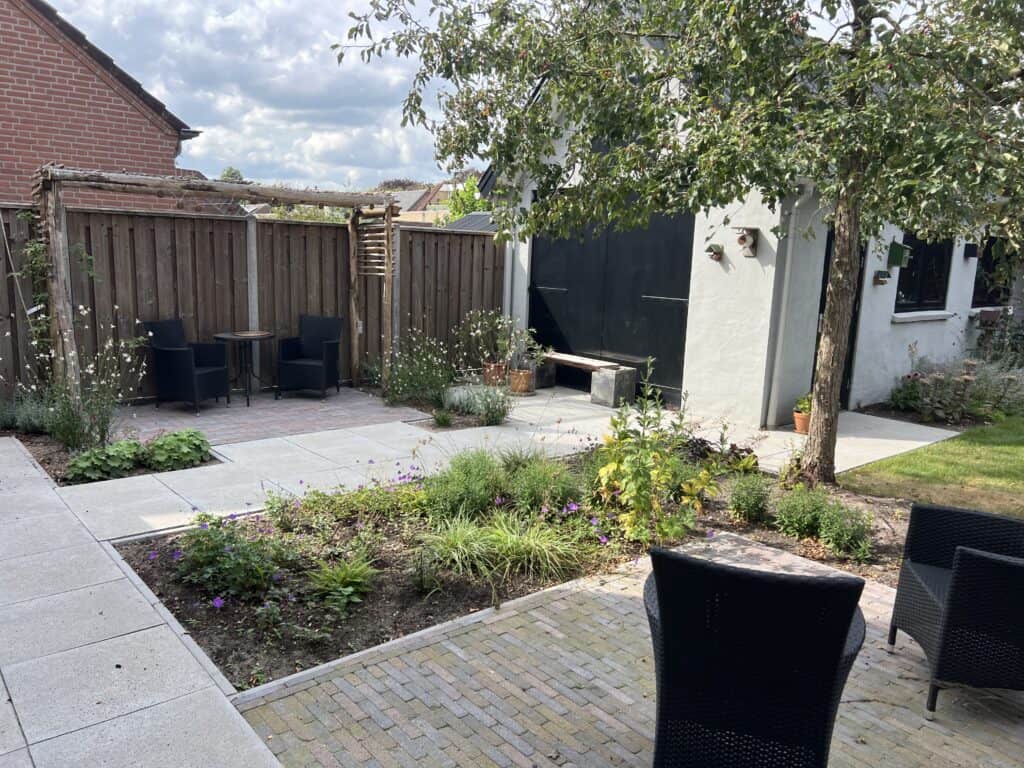 Gezellig tuin met terras, grote boom, watertafel en loungeplek, perfect voor ontspanning en tuinontwerp.