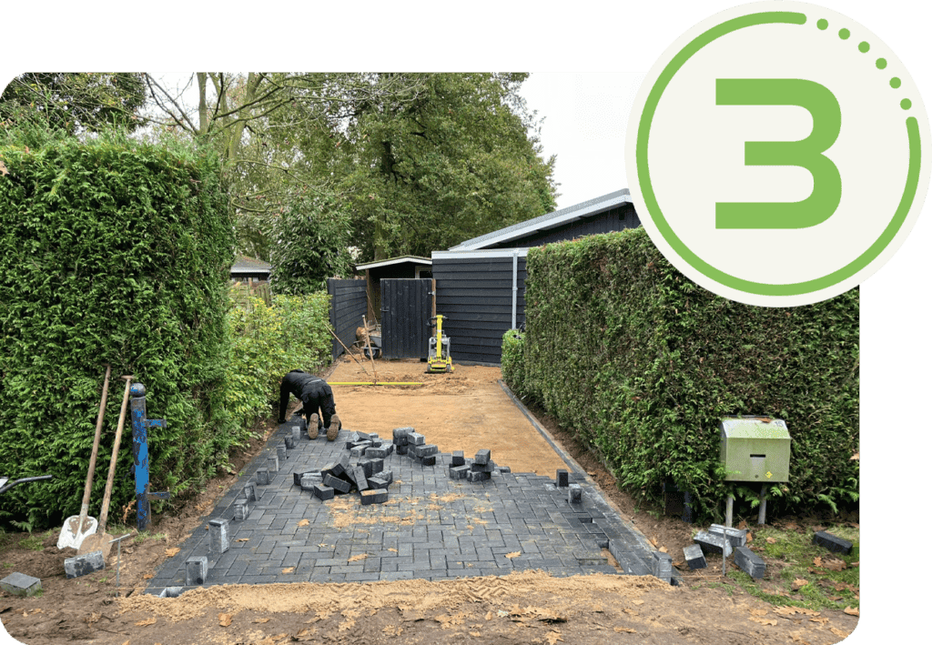 Zwart betegeld tuinpad in aanleg met hovenier, groene heggen en bouwmaterialen.