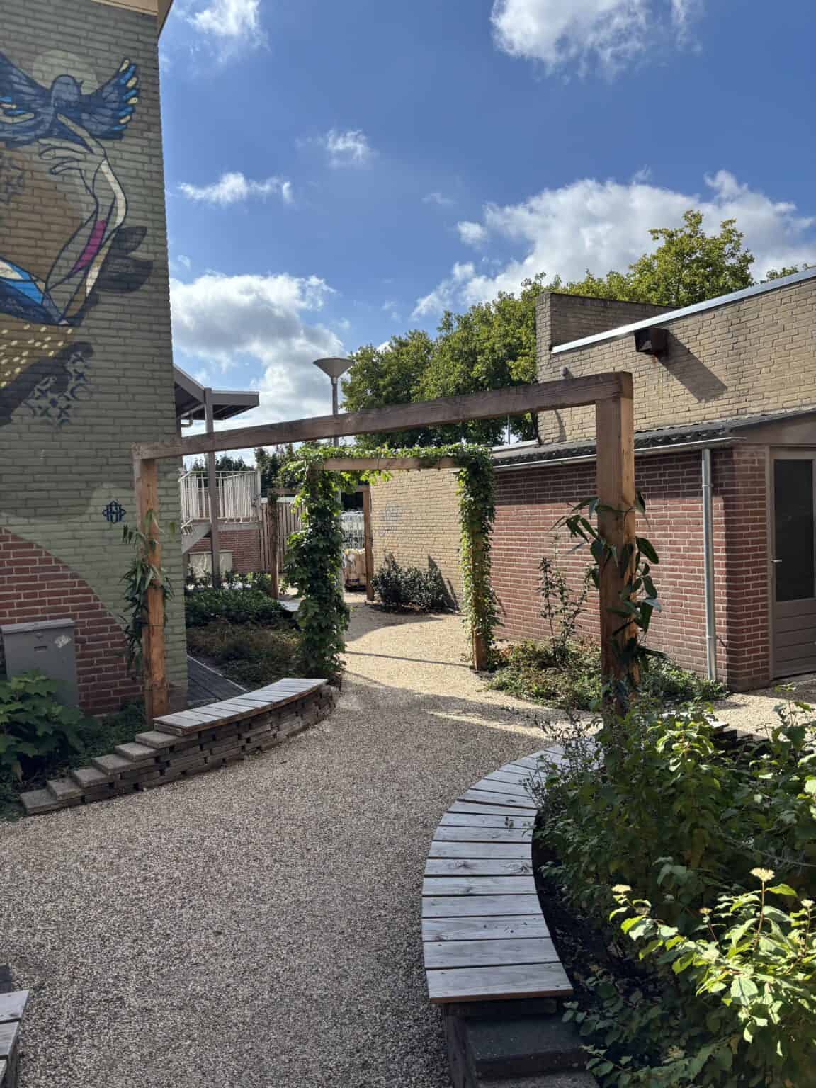 Kunstmatige tuin met houten pergola, groene planten en zitbanken op grindpad.