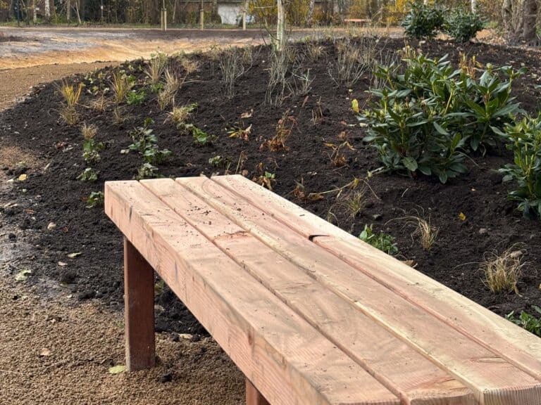 Steigerhouten tuinbank met bloeiende vaste planten en struiken op verse tuinbedden.